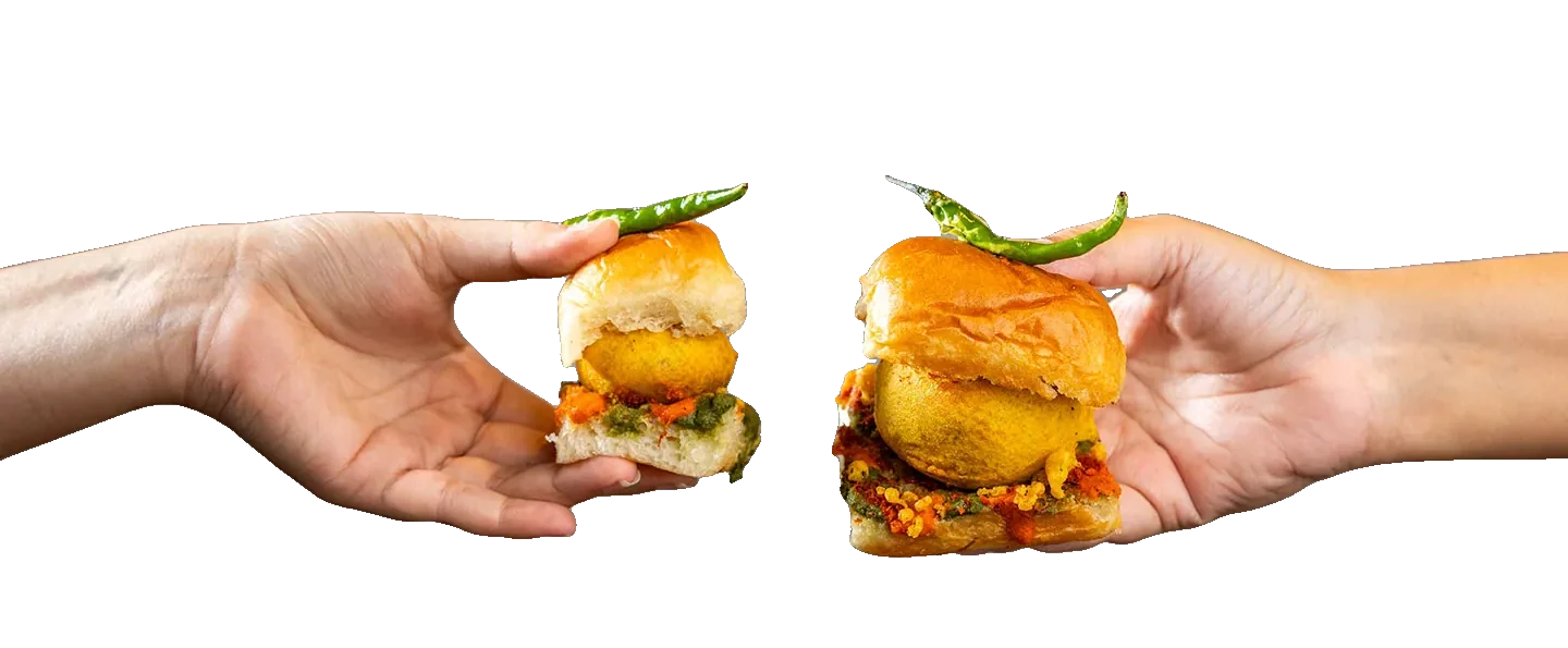 Two hands raising a mini vada pav and a large vada pav towards each other, like a toast